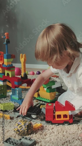 Little cute boy sitting floor enjoying toys at home. Baby designer, game, baby, playing, focused, at home, family, curly hair colored toys lego designer cars children's track Contemporary design.