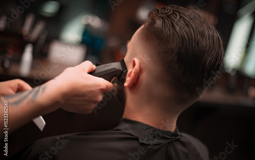 A barber uses clippers to trim a client's beard and neckline in a modern barbershop, showcasing precision grooming and clean styling in a professional setting..