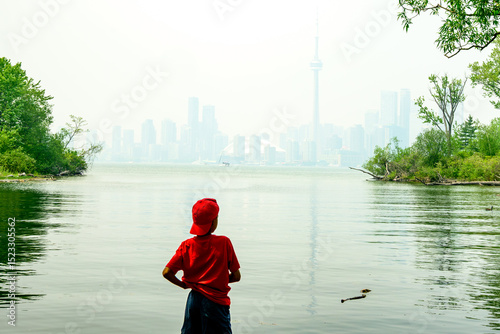 Wild fire smoke over a big city: a young person looks out from the Toronto Islands at the downtown skyline wrapped in diffuse smoke haze at midday room for text shot June 6, 2025