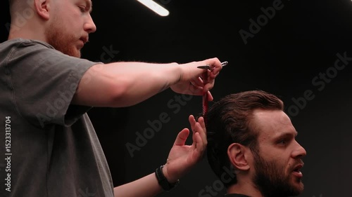 Professional barber trimming a male client's hair with precision scissors in a contemporary barbershop setting. Barber focused, client relaxed. Stylish grooming scene with a dark background.