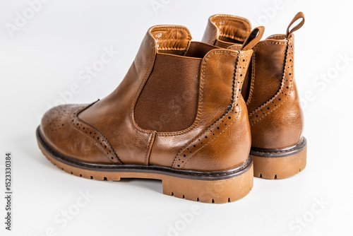 Pair of brown leather Chelsea boots with brogue detailing and rubber sole on a white background