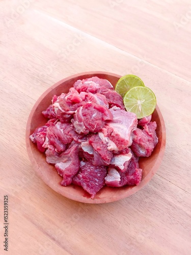 raw minced meat. raw goat meat served with lime on a wooden plate on a wooden background.