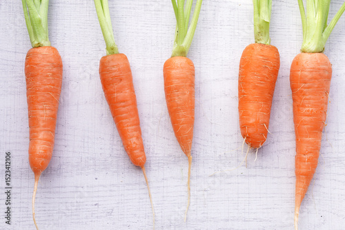 Organic mini carrots with leaves isolated on white wood background.