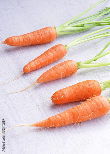 Organic mini carrots with leaves isolated on white wood background.