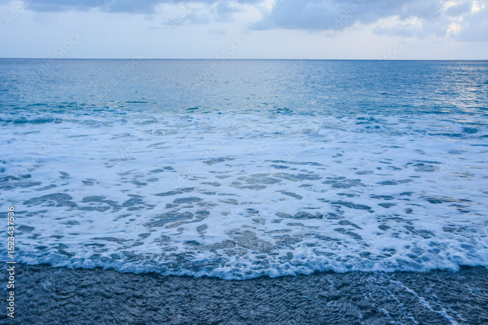 Obraz premium Turbulent Waves Meeting a Dark Pebble Shoreline: A dynamic scene of foamy ocean waves reaching a beach composed of dark pebbles. Coastal Scene: dark pebbles and foaming ocean waves.