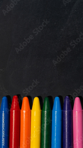 Colorful wax crayons aligned at the bottom of a blackboard with empty space above ready for text or creative back to school designs. 
