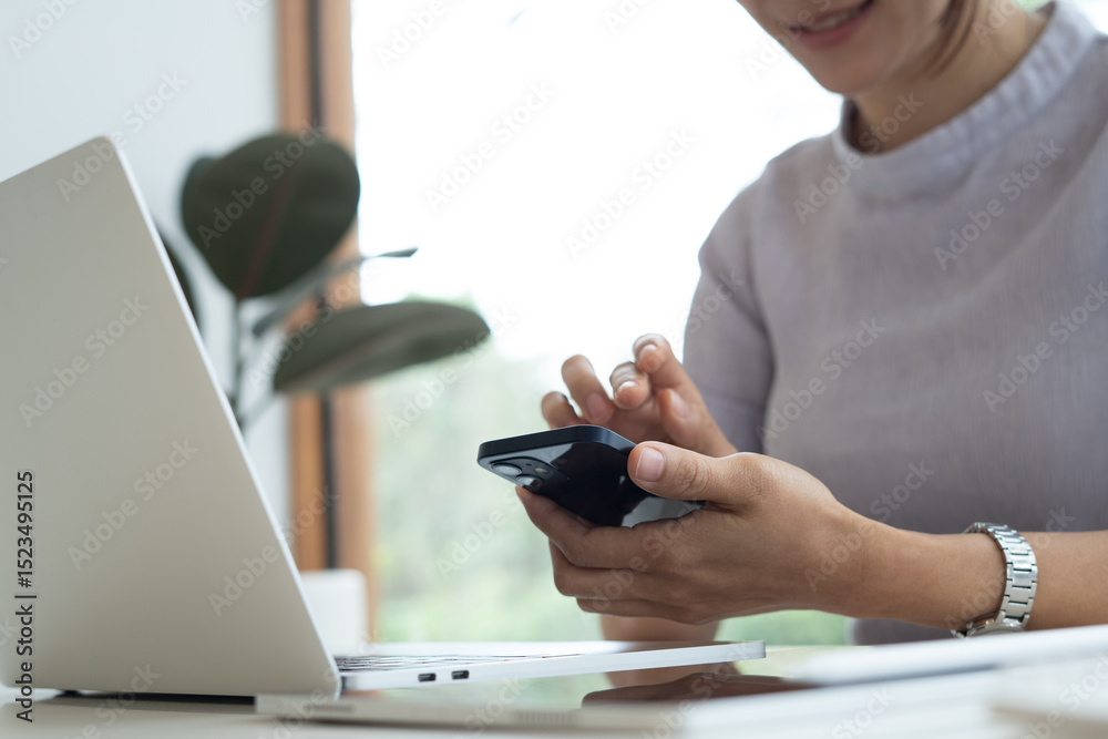 Fototapeta premium Woman using smartphone during working on laptop computer at coffee shop or home office. Casual business woman using smartphone and laptop browsing the internet or social networking, remote work