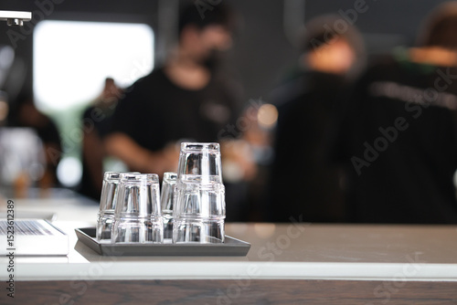 A small glass of water is placed upside down on the table. Clean drinking glasses are placed on the counter for use.