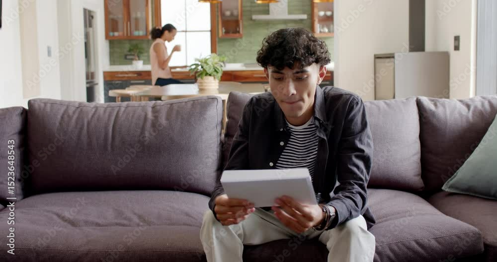 Diverse mother and son opening envelope and unfolding letter on gray sofa sharing exciting news Diverse mother and son opening envelope and unfolding letter on gray sofa sharing exciting news