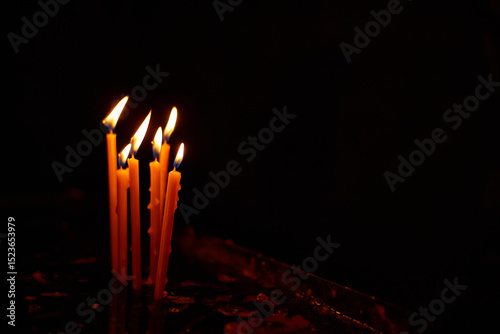 Row of burning candles in a dark church interior, creating a peaceful and spiritual atmosphere. Warm candlelight contrasts with the deep shadows, symbolizing prayer, hope, and remembrance.