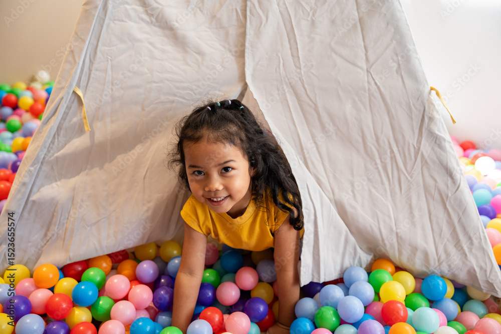 Obraz premium A happy little girl plays with a ball in a colorful ball pit, enjoying the fun and enhancing her development through playful activities and exercise..
