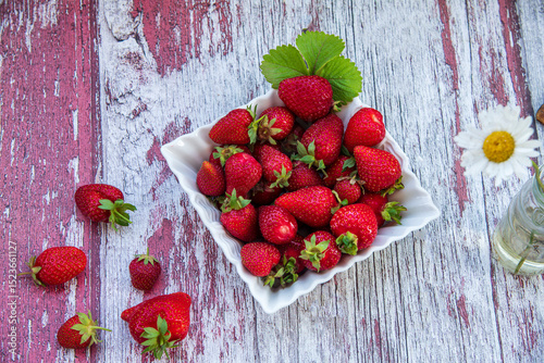 Delicious ripe organic strawberries in a white plate on a wooden table.
