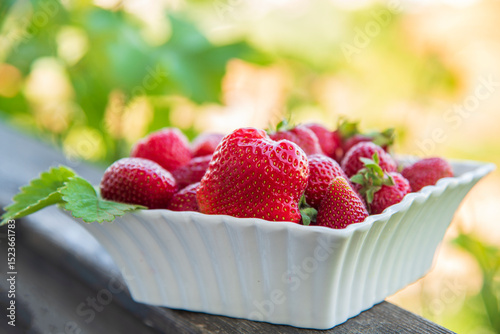 Delicious ripe organic strawberries in a white plate on a wooden table.