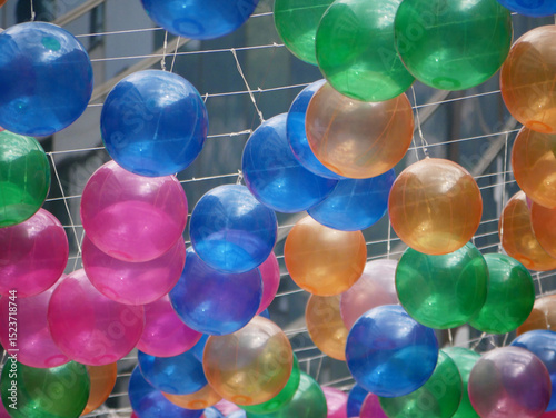 Fototapeta Naklejka Na Ścianę i Meble -  Ocean of colorful balloons hanging on a net high in an urban street above a walkway