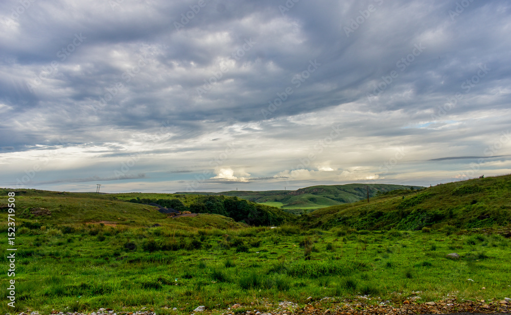 Obraz premium A dramatic cloudy sky with patches of blue over a green mountainous landscape in Meghalaya. 
