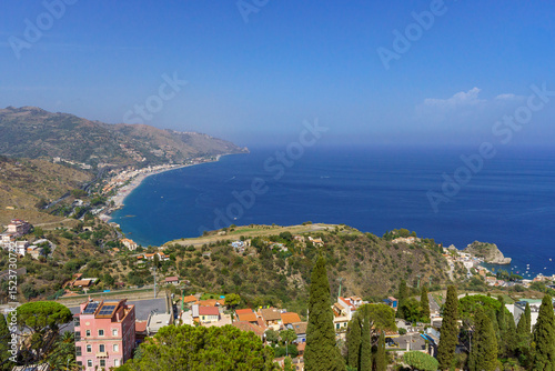 Fototapeta Naklejka Na Ścianę i Meble -  Aerial view over Taormina and its coastline with its city beaches and a deep blue sea and sky on a beautiful and sunny day in Sicily, Italy  