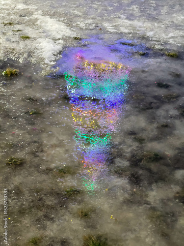 A bright reflection of festive lights in a puddle on a winter New Year's Eve. The side, illuminated by the reflection of the lights of the Christmas tree.