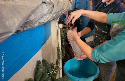 Hands pour holy Epiphany water from a tap in a church into a plastic bottle.