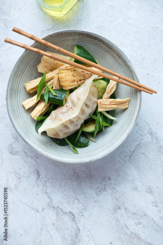 Plate with tofu skin, smashed cucumber salad and pork dumpling, vertical shot on a white stone background with space, flat lay