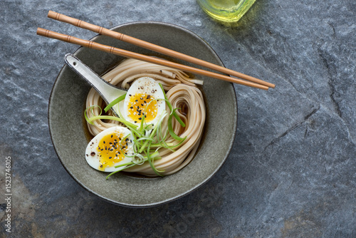 Bowl of miso udon with boiled egg on a dark-grey granite background, horizontal shot with space, top view