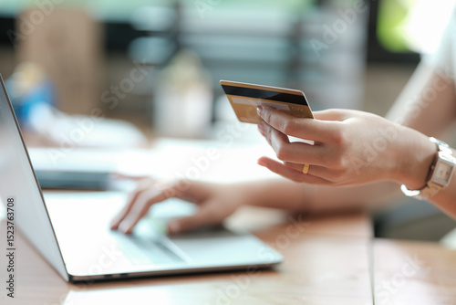 Online Shopping And Easy Payment. Close-up cropped view of a woman holding a credit card and using a personal computer, typing on laptop keyboard, checking banking account, focus on hand.
