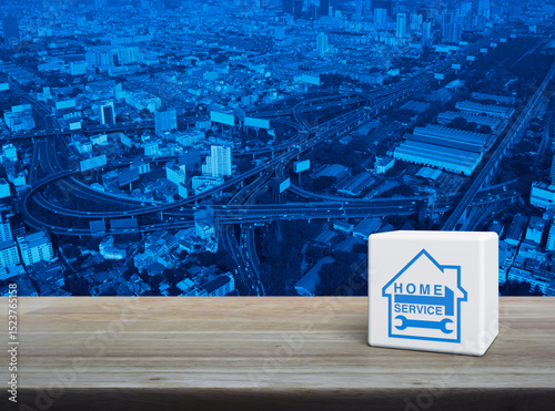 Hammer and wrench with house icon on white block cube on wooden table over modern city tower, street, expressway and skyscraper, Business home service concept