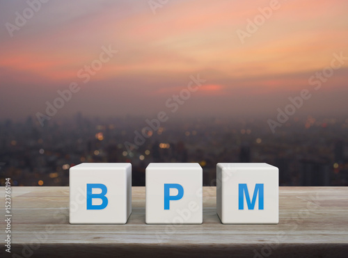 BPM acronym on white block cubes on wooden table over blur of cityscape on warm light sundown, Business process management concept