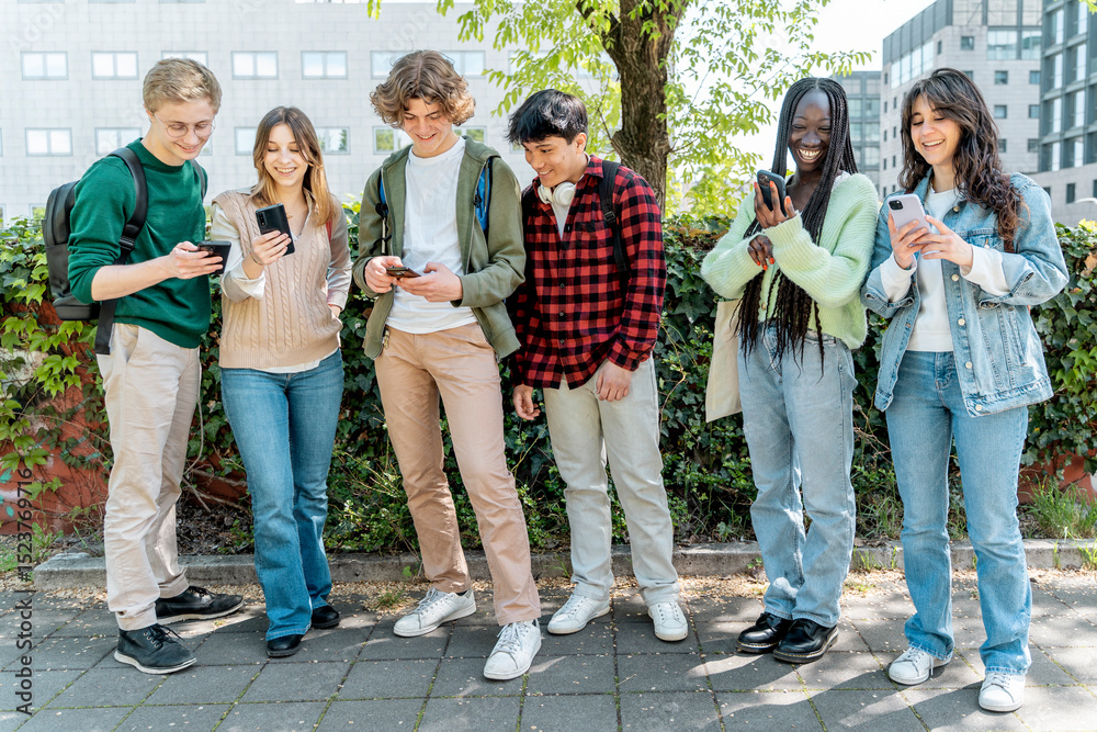 Fototapeta premium Group of diverse high school students using smartphones outdoors during break in urban school setting