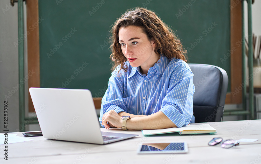 Female online teacher looking at laptop talking on virtual distance class in classroom or webinar web training working in office. Young business woman leading hybrid conference online video call. Female online teacher looking at laptop talking on virtual distance class in classroom or webinar web training working in office. Young business woman leading hybrid conference online video call.