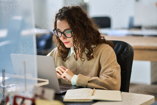 Busy young professional business woman employee or student wearing glasses using laptop watching online webinar or training web course, looking at computer, thinking, doing research working in office.