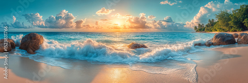 Panoramic view of waves crashing on sandy beach with granite rocks at vibrant sunrise over tropical ocean coast with blue sky and scattered clouds