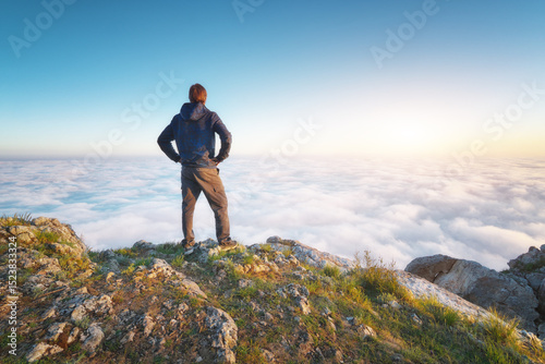 Man stands over the cover clouds on the edge of the abyss and looks on sun.