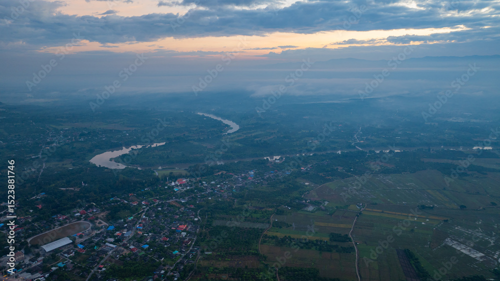 Fototapeta premium A stunning aerial view of a winding river flowing through a vast rural landscape at dawn. The soft morning light and misty atmosphere create a tranquil and picturesque scene, with scattered villages