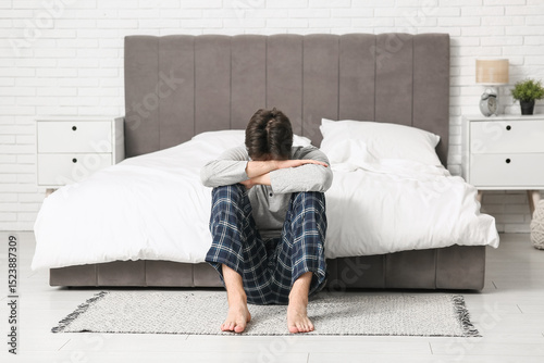 Depressed young man sitting on carpet in bedroom
