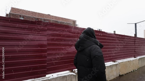 Young Woman in Cozy Winter Outfit Strolling Along City Construction Site on Cold Snowy Day with Modern Architecture in Background