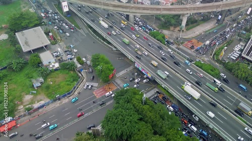 This aerial footage shows heavy traffic on a Jakarta highway. Cars, trucks, and motorcycles are moving along the road. There are trees and buildings visible in the surrounding area.