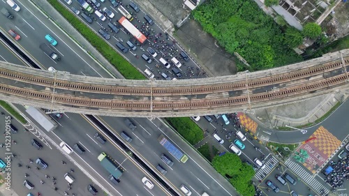 Aerial shot of a busy highway in Jakarta, Indonesia. Cars, trucks, and motorcycles are stuck in heavy traffic. An old train track runs overhead.