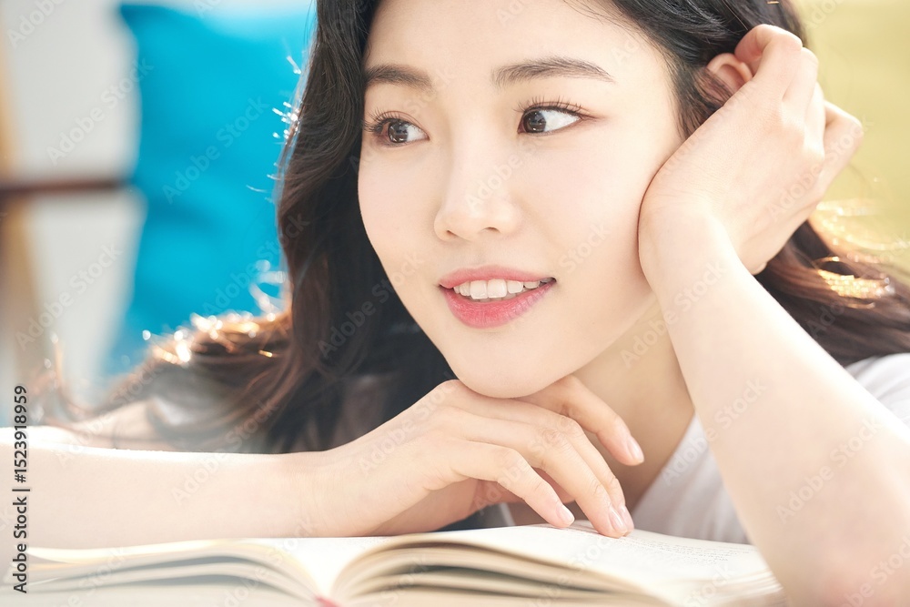 Fototapeta premium Tired Young Female Student Resting Head on Open Book at Desk in Bright Living Room