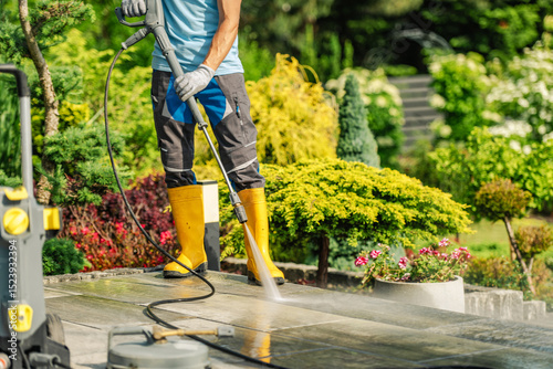 Man Cleans Patio With Pressure Washer on a Sunny Day in a Landscaped Garden