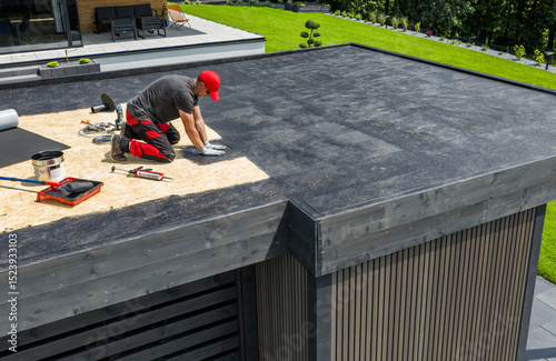 Worker Installing EPDM Roofing Material on a Residential Flat Roof During a Sunny Day