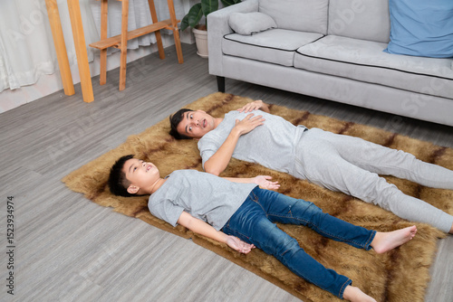 Asian handsome single father and his elementary school son lie down on tiger-patterned carpet in living room together. Talking and spending time with adorable boy with happy during the holidays.