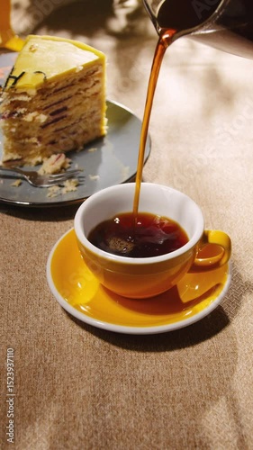 Pouring coffee into yellow ceramic cup with the cake on background