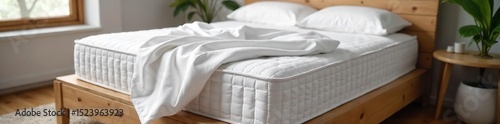 A plush, new mattress sits on a wooden platform, ready for a comfortable night's sleep The crisp white sheets are neatly tucked in, highlighting the inviting texture of the mattress , new, luxury