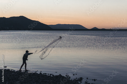 Young fisherman throwing net at sunset on the shore