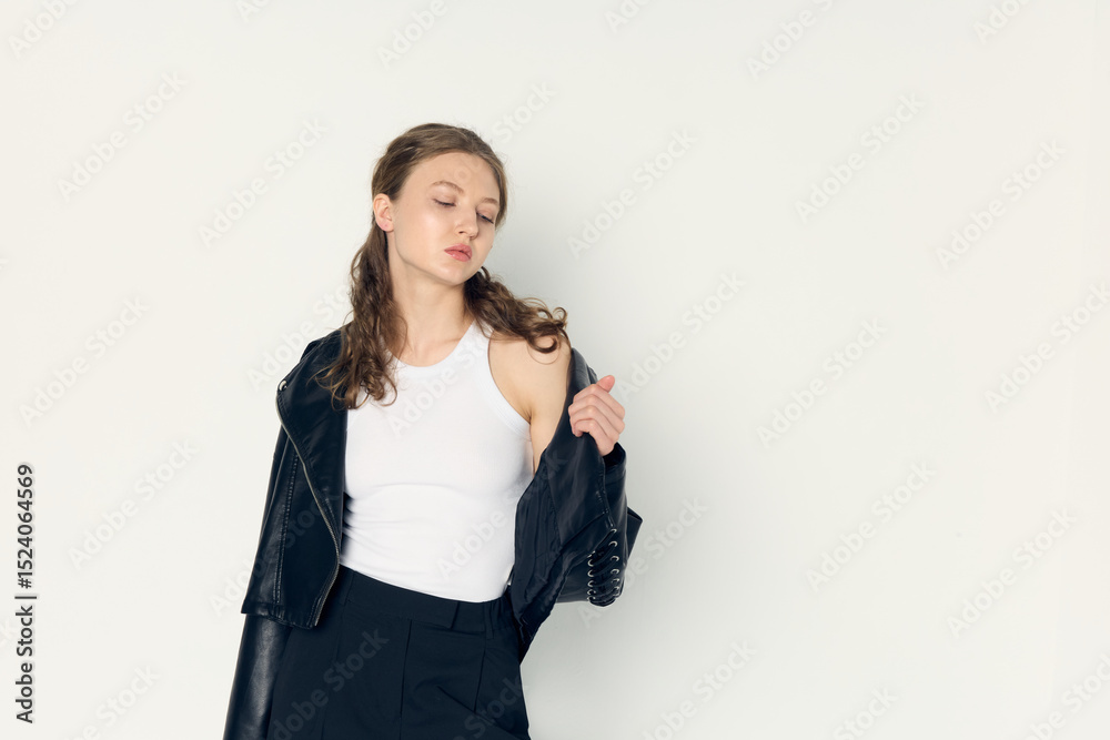 A stylish curly-haired woman poses against a light background in a fashionable jacket and a white T-shirt A stylish curly-haired woman poses against a light background in a fashionable jacket and a white T-shirt