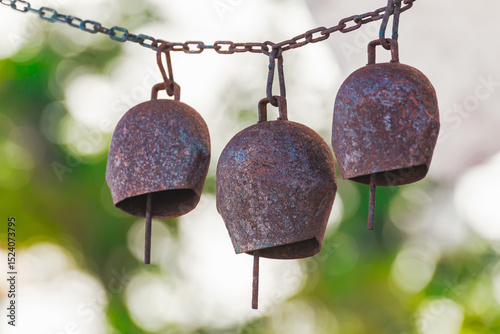 Rusty iron bells hanging on a chain with blurred green background, rustic outdoor decor