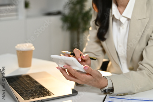A woman is sitting at a desk with a laptop and a calculator. She is using the calculator to do some calculations