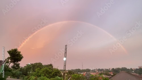 Rainbow in the evening sky after rain, a semicircular rainbow in the distance above the roof of a house