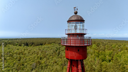Red lighthouse stands tall above green forest on Ruhnu Island, Estonia during bright daylight