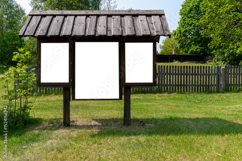 Information board stands empty in a grassy area near a wooden fence on a sunny day
